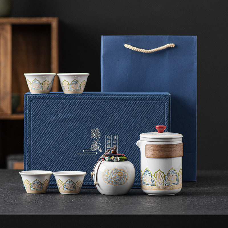 Tea set with ceramic teapot and cups in front of a blue gift box on a dark surface.