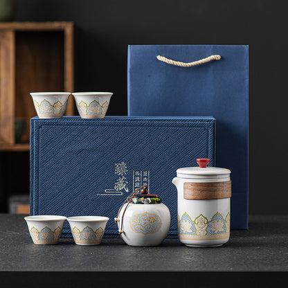 Tea set with ceramic teapot and cups in front of a blue gift box on a dark surface.