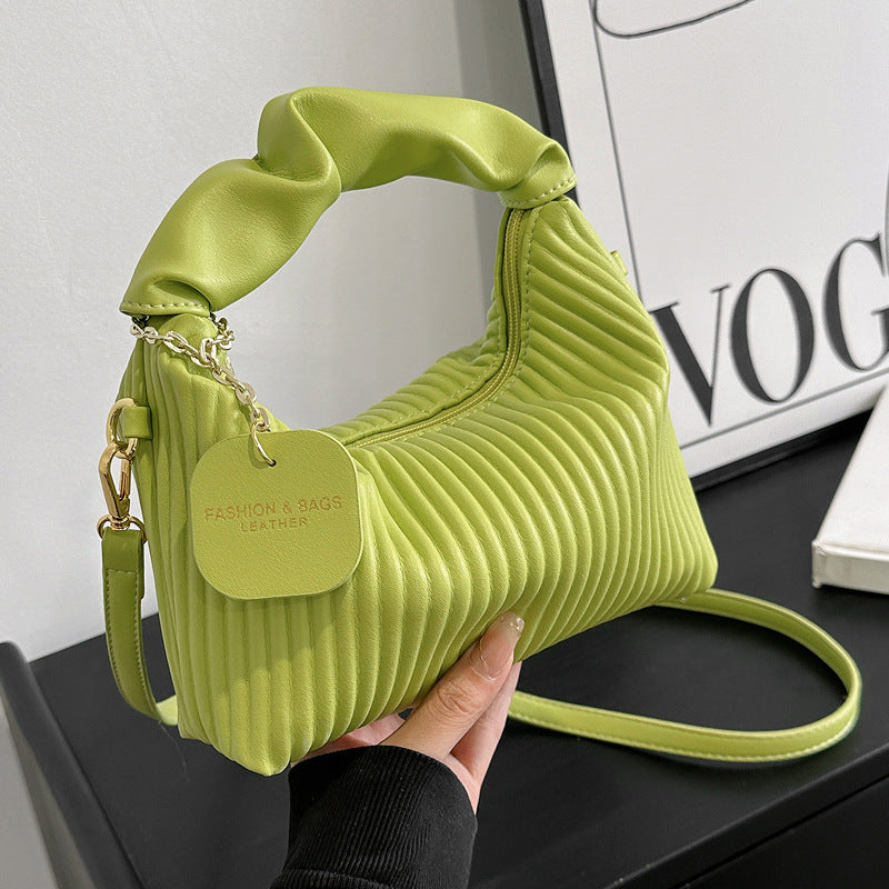 Green pleated handbag held by a hand with a 'Fashion & Bags' tag, against a blurred background.