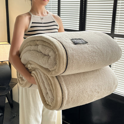Person holding a folded beige blanket with a brand label indoors.