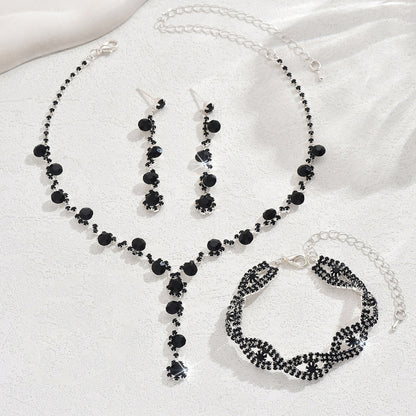 Black beaded jewelry set including necklace, earrings, and bracelet on a white fabric background