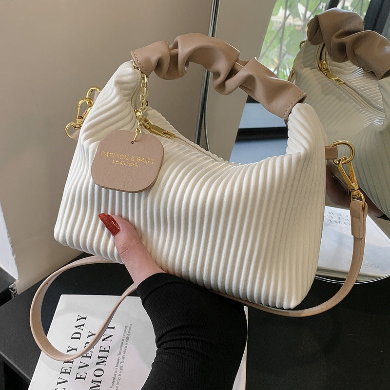 Beige textured handbag with ruffled handles held by a person, placed on a surface with a magazine underneath.