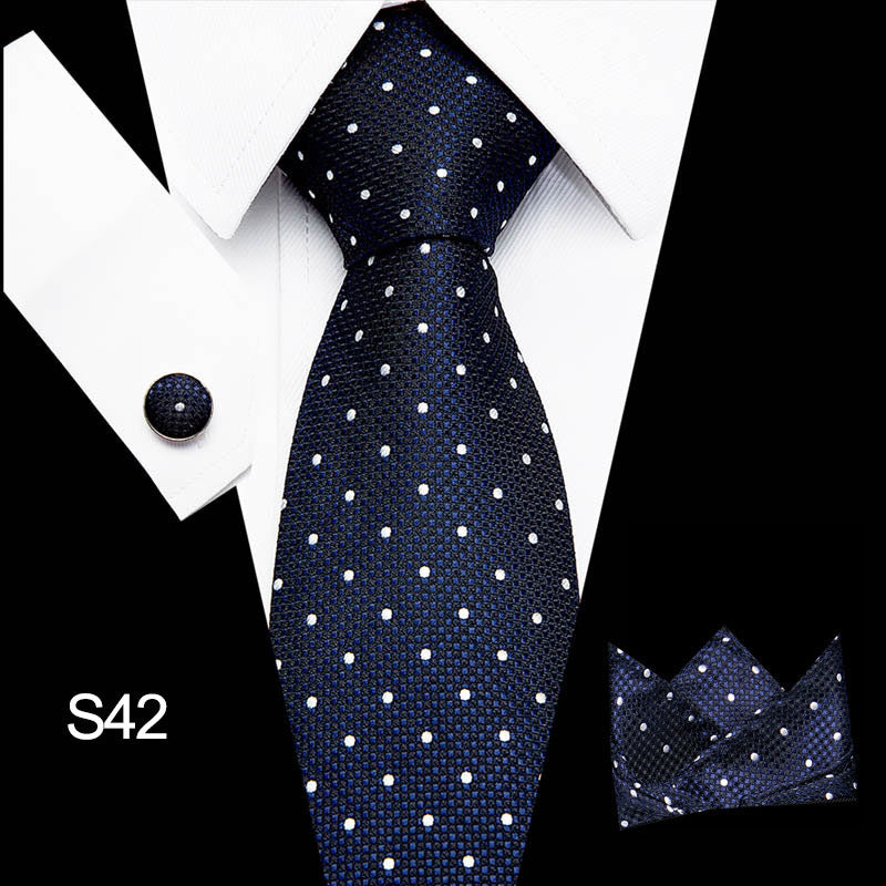 Navy blue tie with white polka dots, matching pocket square, and cufflink on a white shirt.