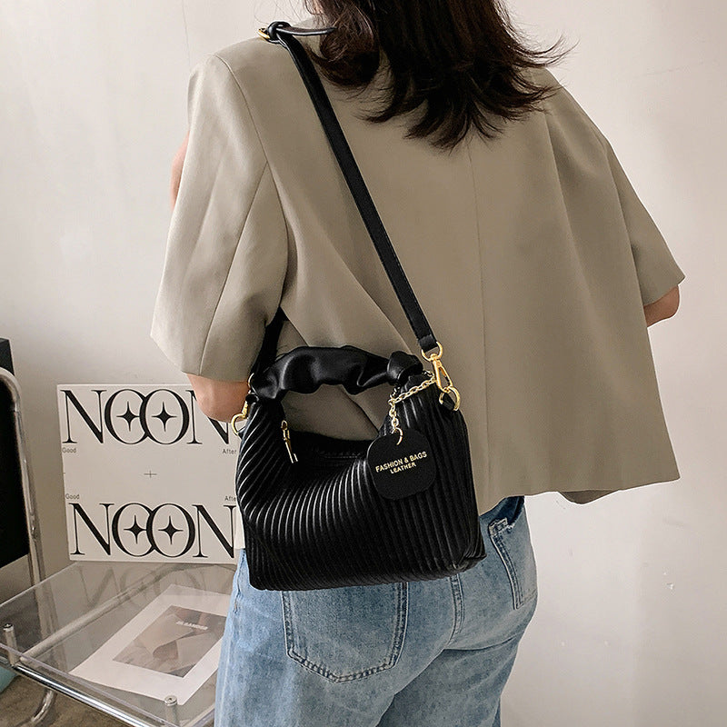 Person wearing a black handbag with gold chain detail, standing in front of a white wall with 'Neon' branding.
