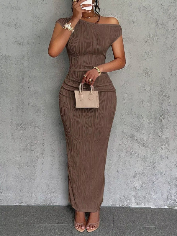 Woman wearing a brown off-shoulder dress against a gray concrete wall.
