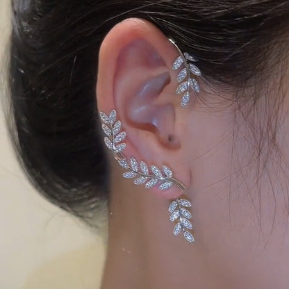 Silver leaf-shaped earring worn on an ear with a neutral background