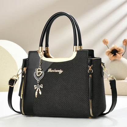 Black small square crossbody bag with top handles and gold zipper, heart and bow charm