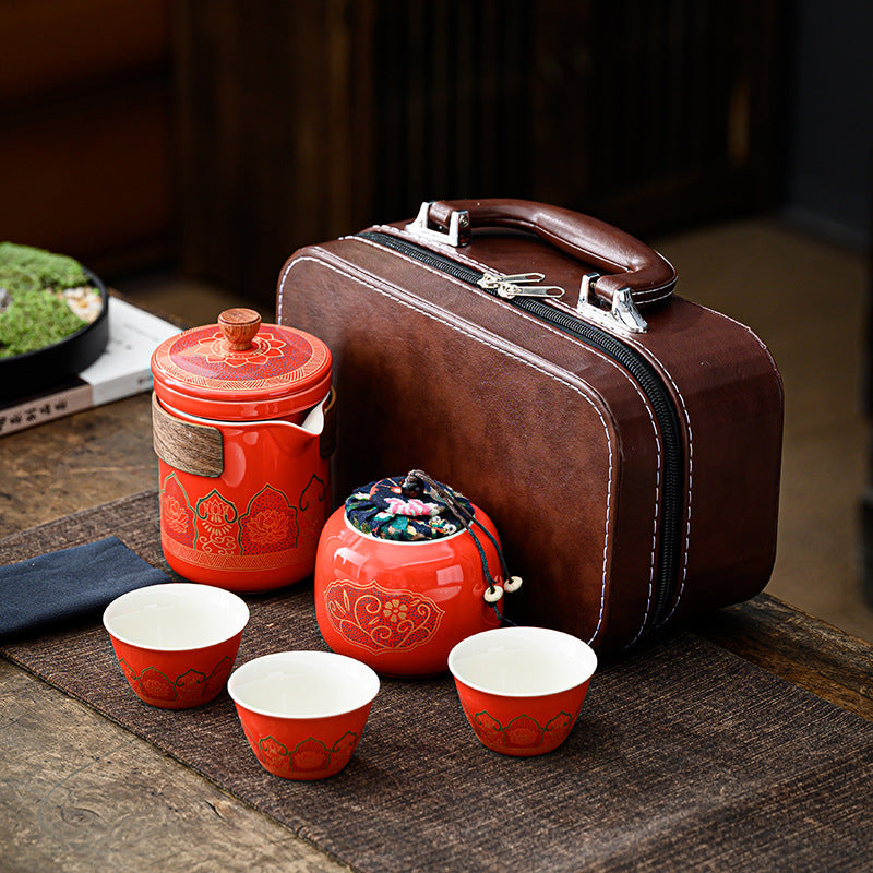 Red ceramic tea set with a brown suitcase on a wooden surface