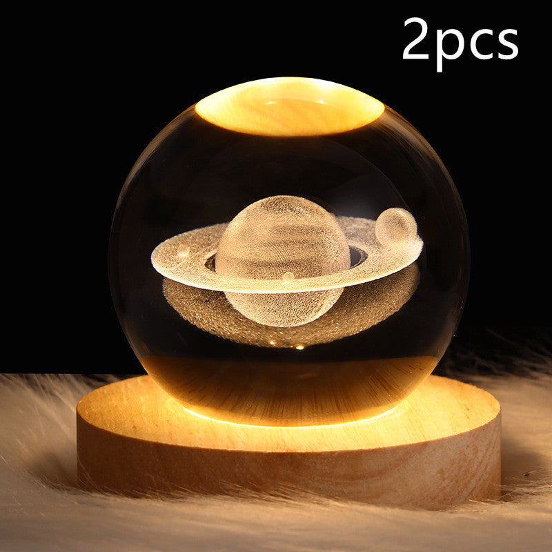 Two levitating Saturn models in a glass sphere on a wooden base with a dark background.