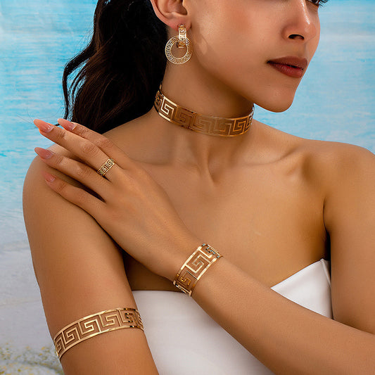Woman wearing gold jewelry including earrings, choker, ring, and bracelet against a blue and white background.
