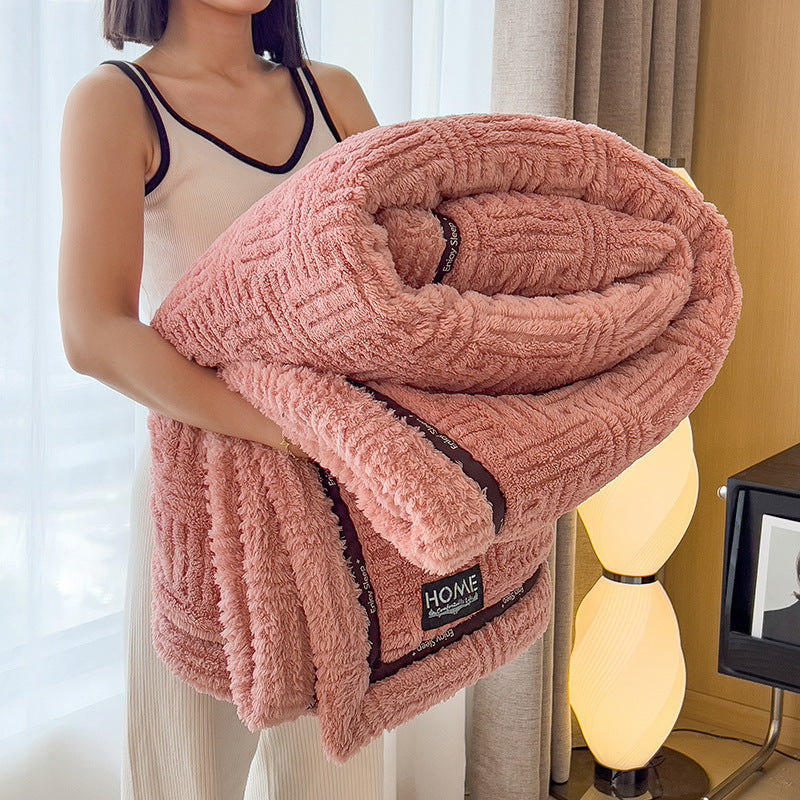 Person holding a pink textured blanket with 'HOME' label in a room setting.