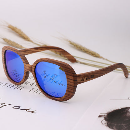 Wooden sunglasses with blue lenses on a white surface with dry grass.