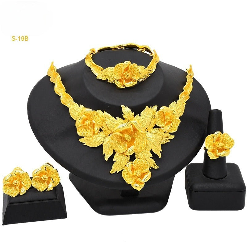 Gold jewelry set including necklace, bracelet, ring, and earrings on a black stand.