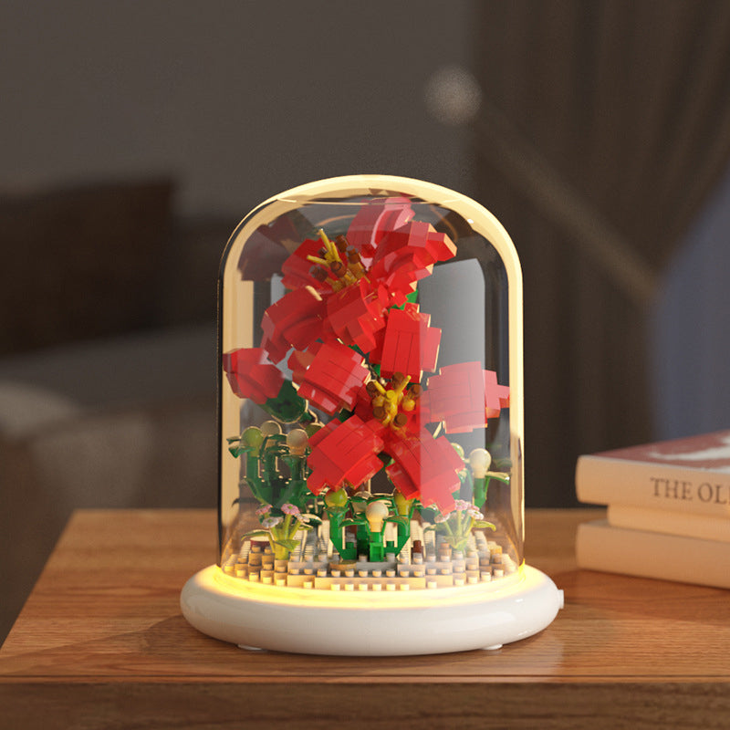 Decorative lamp with a glass cover featuring a red flower and small figures on a wooden surface.