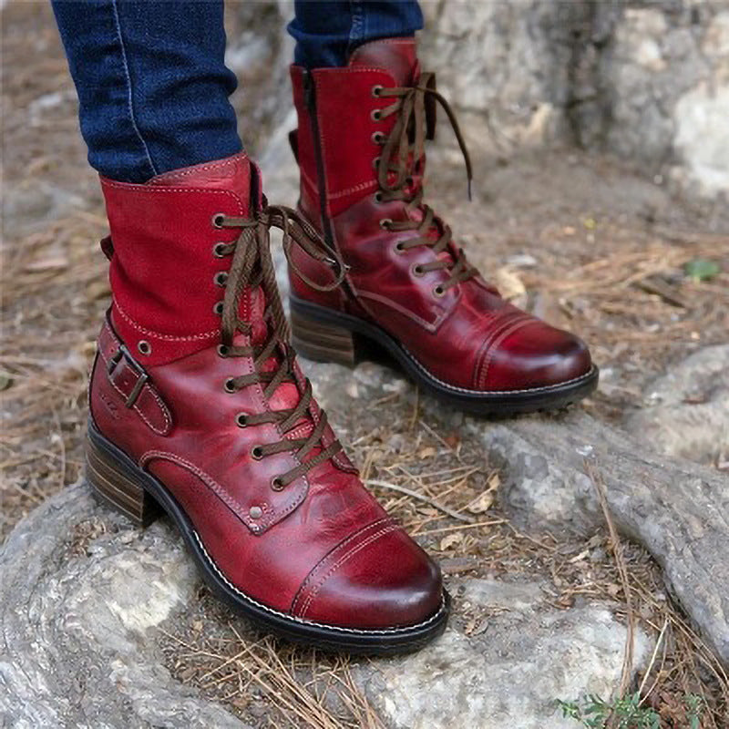 Red leather boots with brown laces worn by a person on a stone surface.