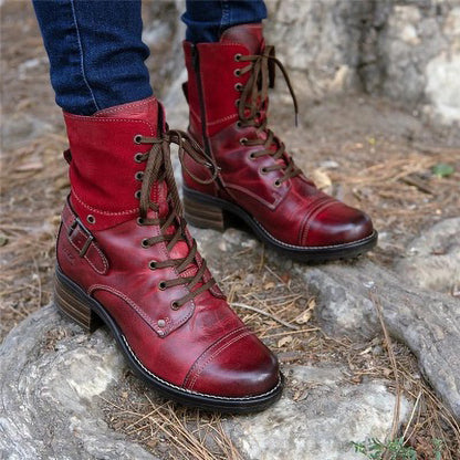 Red leather boots with brown laces worn by a person on a stone surface.