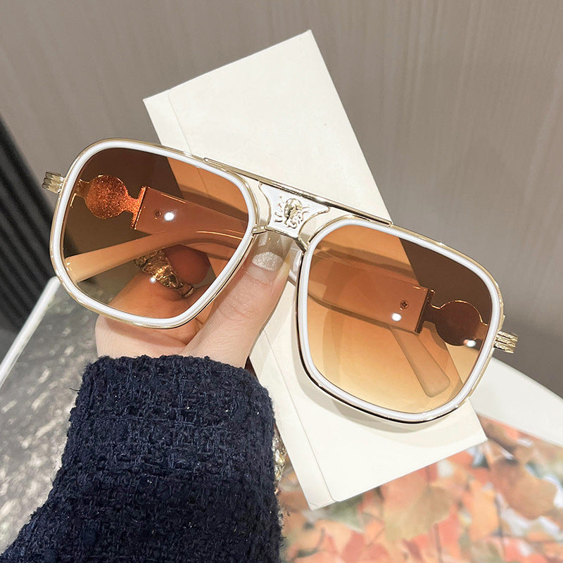 Gold-framed sunglasses with brown lenses held by a hand on a white background