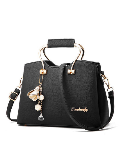 Black handbag with gold accents and floral charm on a white background