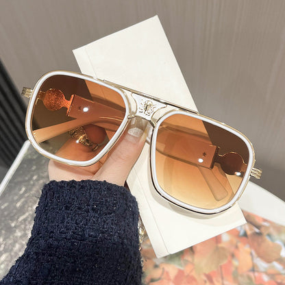 Gold-framed sunglasses with brown lenses held by a hand on a white background