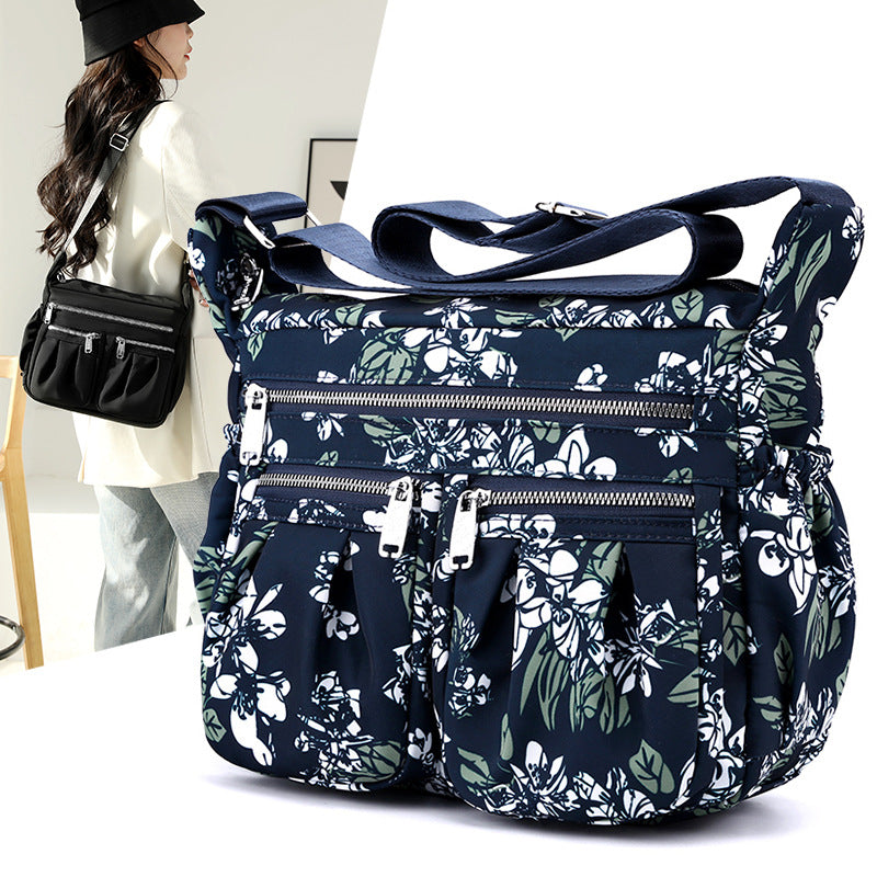 Large-capacity crossbody bag in blue botanical print with multiple front zip compartments.