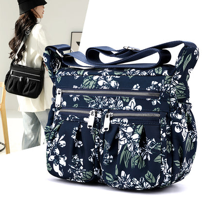 Large-capacity crossbody bag in blue botanical print with multiple front zip compartments.