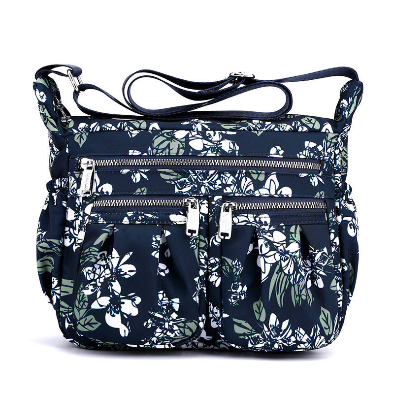 Large-capacity crossbody bag in navy floral print with multiple zip pockets and handles.