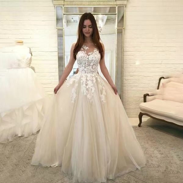Woman wearing a white lace evening gown in a room with a couch and mirror.