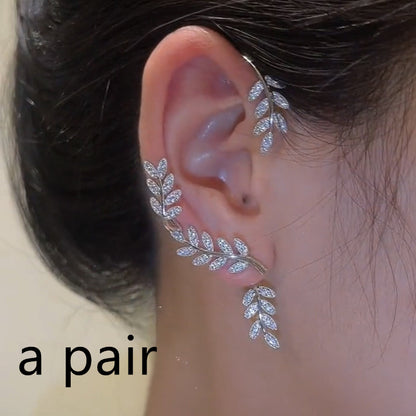 Silver leaf-shaped earring worn on an ear with a neutral background