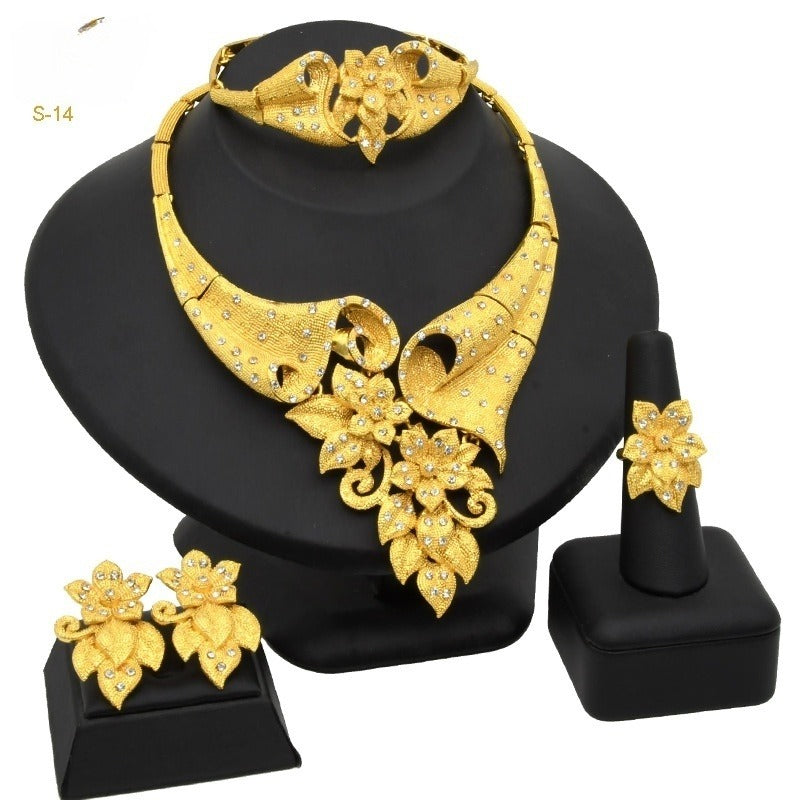 Gold jewelry set including necklace, earrings, and ring on a black stand.
