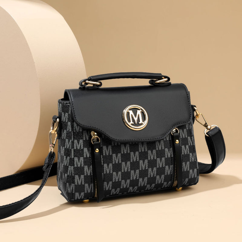 Black handbag with gold accents and a patterned design on a beige background