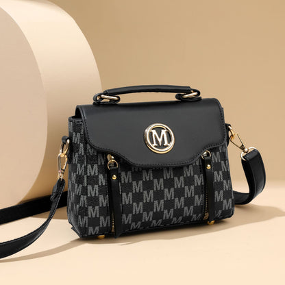 Black handbag with gold accents and a patterned design on a beige background