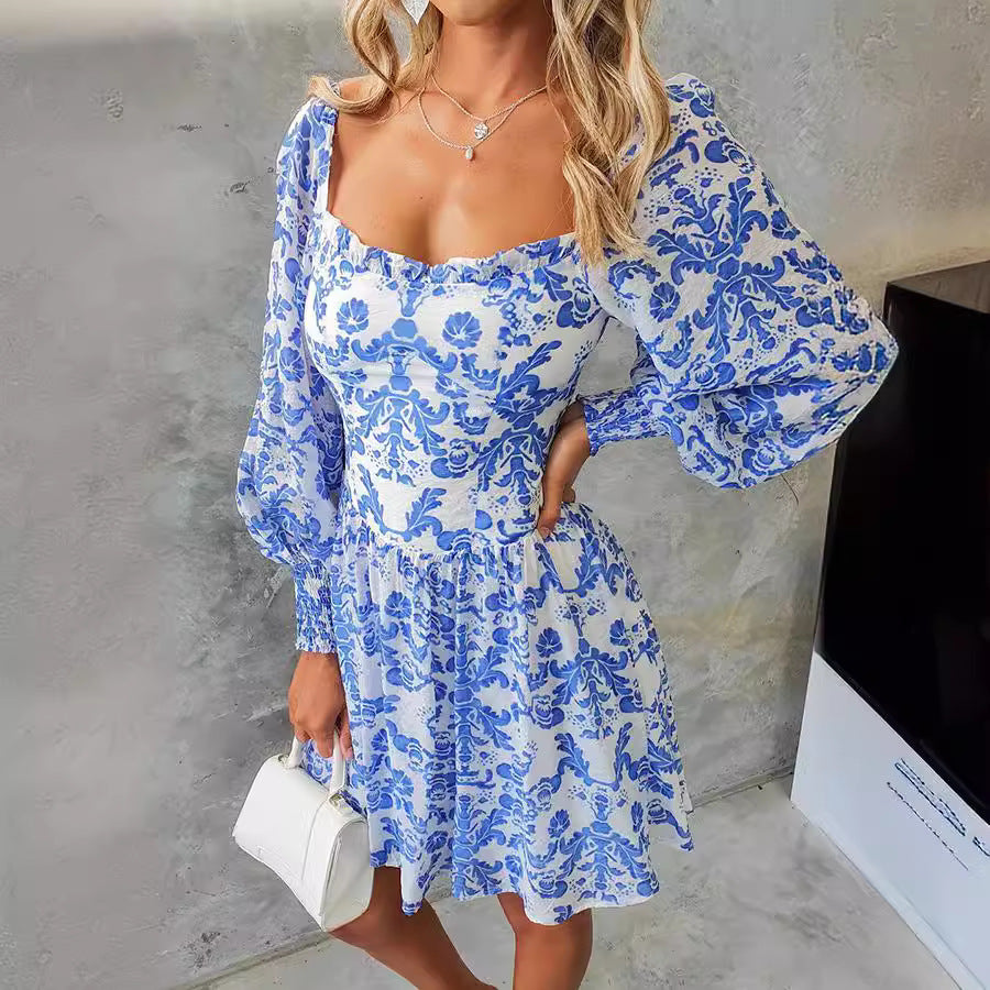 Woman wearing a blue floral dress with long sleeves against a gray wall.