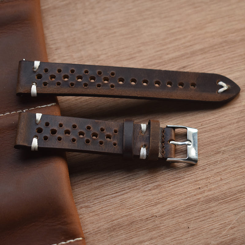 Brown perforated leather watch strap with metal buckle and hole rows, angled view