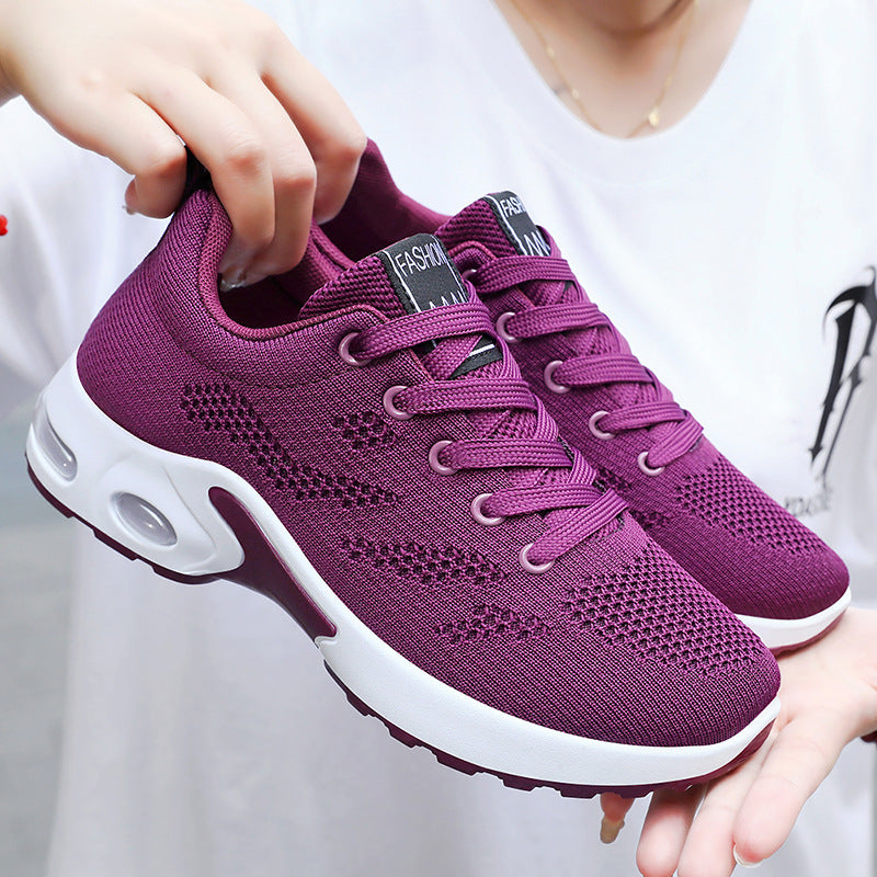 Purple running shoes with white soles held by a person against a white background