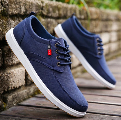 Pair of navy blue sneakers with white soles on a wooden surface.
