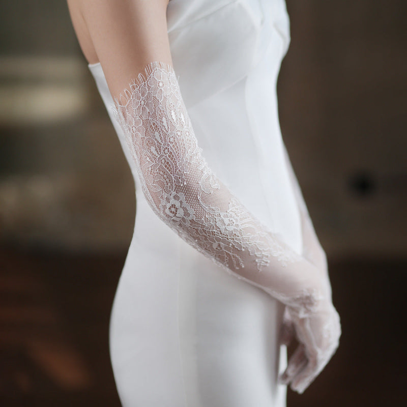 Close-up of a lace glove worn with a white outfit against a blurred background