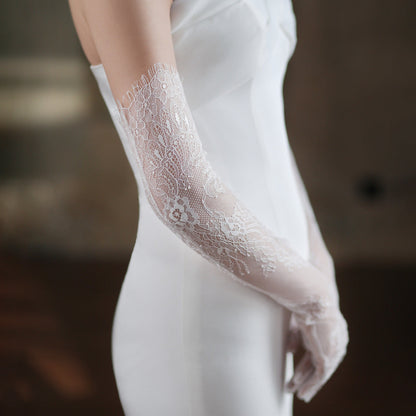 Close-up of a lace glove worn with a white outfit against a blurred background