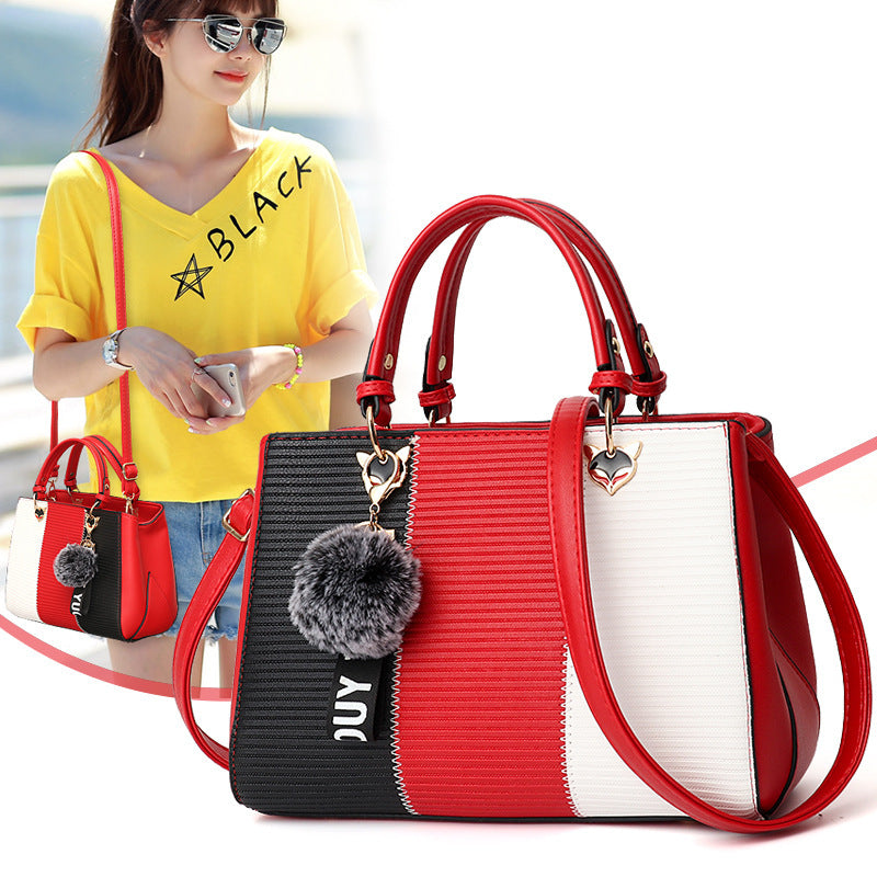 Red and black handbag with a pom-pom charm on a white background