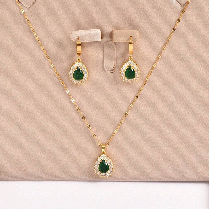 Gold necklace and earrings with green gemstones on a beige background