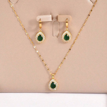 Gold necklace and earrings with green gemstones on a beige background