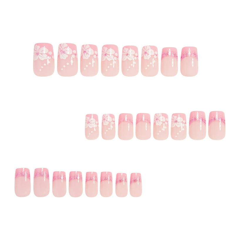 Rows of pink press-on nails with white floral/bow decals and glitter French tips