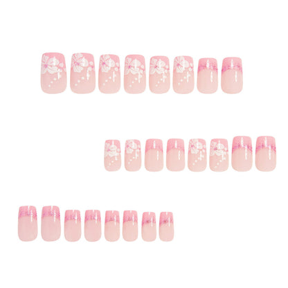 Rows of pink press-on nails with white floral/bow decals and glitter French tips