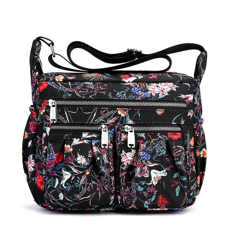 Large-capacity crossbody bag in black floral print with layered front zippers and pockets.
