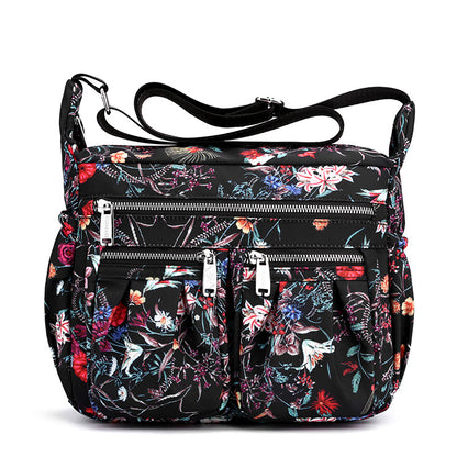 Large-capacity crossbody bag in black floral print with layered front zippers and pockets.