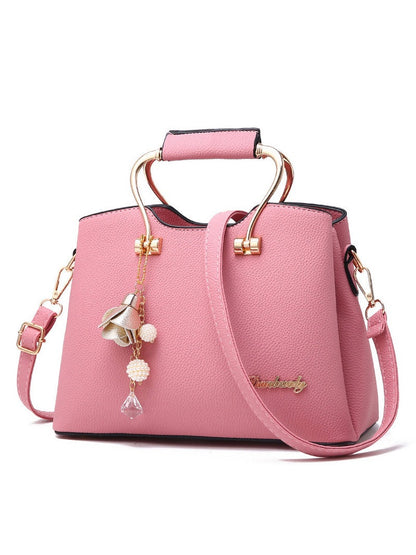 Pink handbag with gold accents and charms on a white background