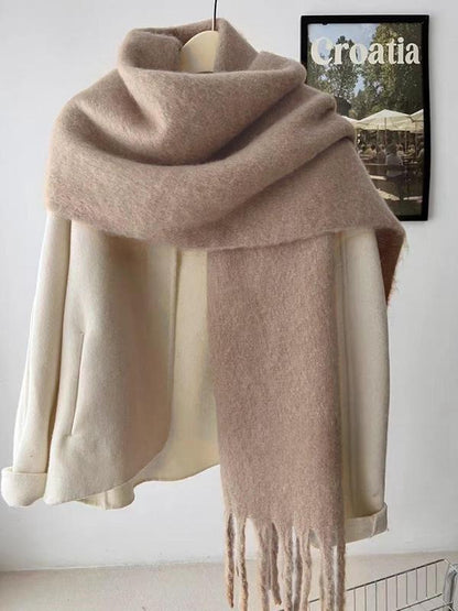Beige scarf with fringe draped over a mannequin against a white wall.