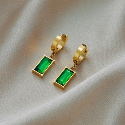 Gold hoop earrings with green gemstones on a beige fabric background