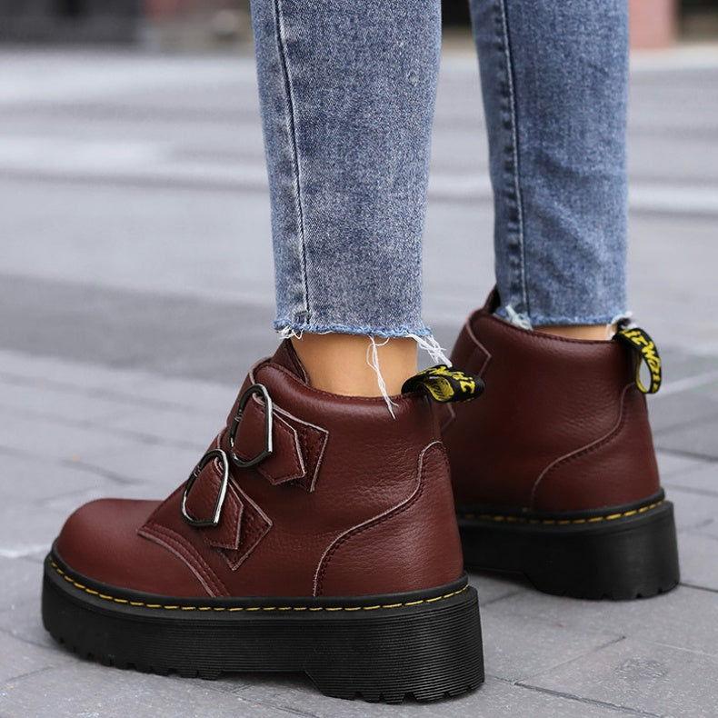 Brown leather boots with black soles worn with blue jeans on a pavement.