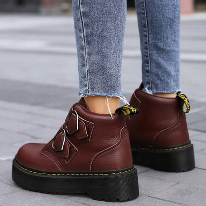 Brown leather boots with black soles worn with blue jeans on a pavement.