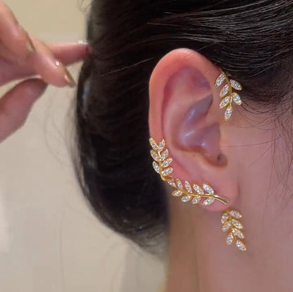Gold leaf-shaped earring being worn on an ear with a neutral background